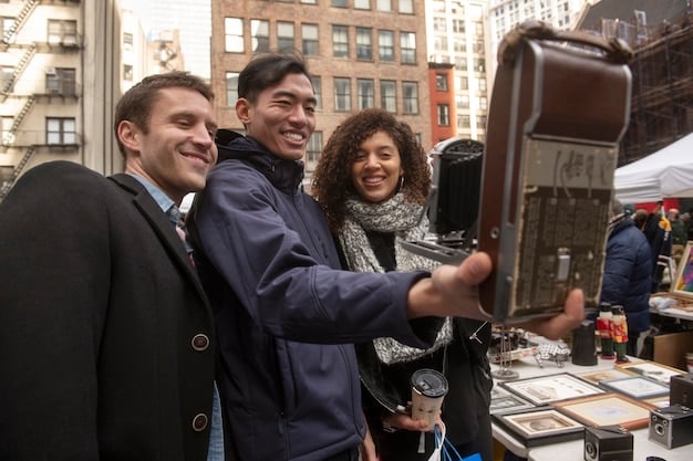 A candid photo of the Enhypen members backstage at a US television show, smiling and posing for the camera. The backdrop includes crew members and production equipment, providing a behind-the-scenes glimpse of their US TV debut experience.
