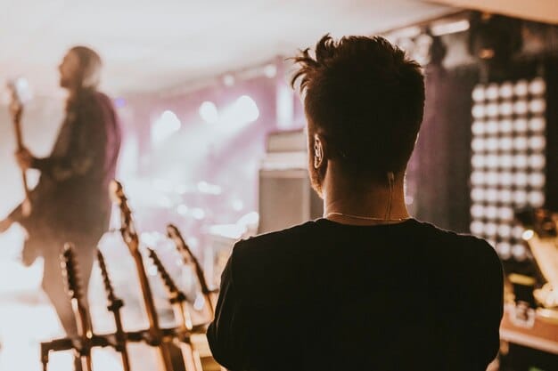 A behind-the-scenes shot of a J-Pop music video set, showing the film crew, complex lighting setup, and a director giving instructions to the idol group members, capturing the intense activity and technical aspects of the production.