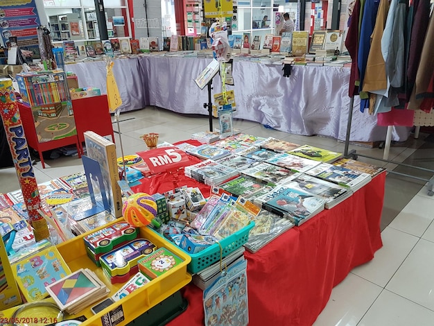 A wide shot of a K-Pop fan convention showcasing various booths selling fan-made merchandise, interactive game stations, and meet-and-greet areas. The atmosphere is energetic and bustling with activity.